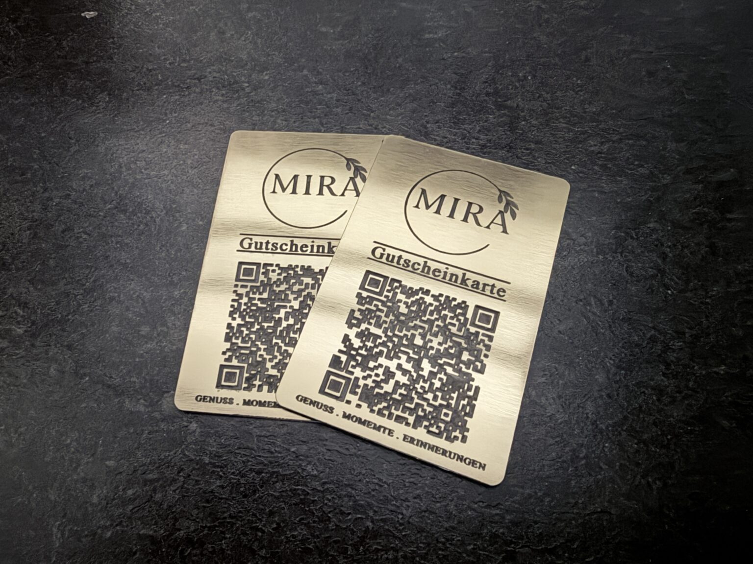 Zwei wiederaufladbare MIRA Gutscheinkarten aus gebürstetem Gold-Metall mit Logo-Gravur und QR-Code