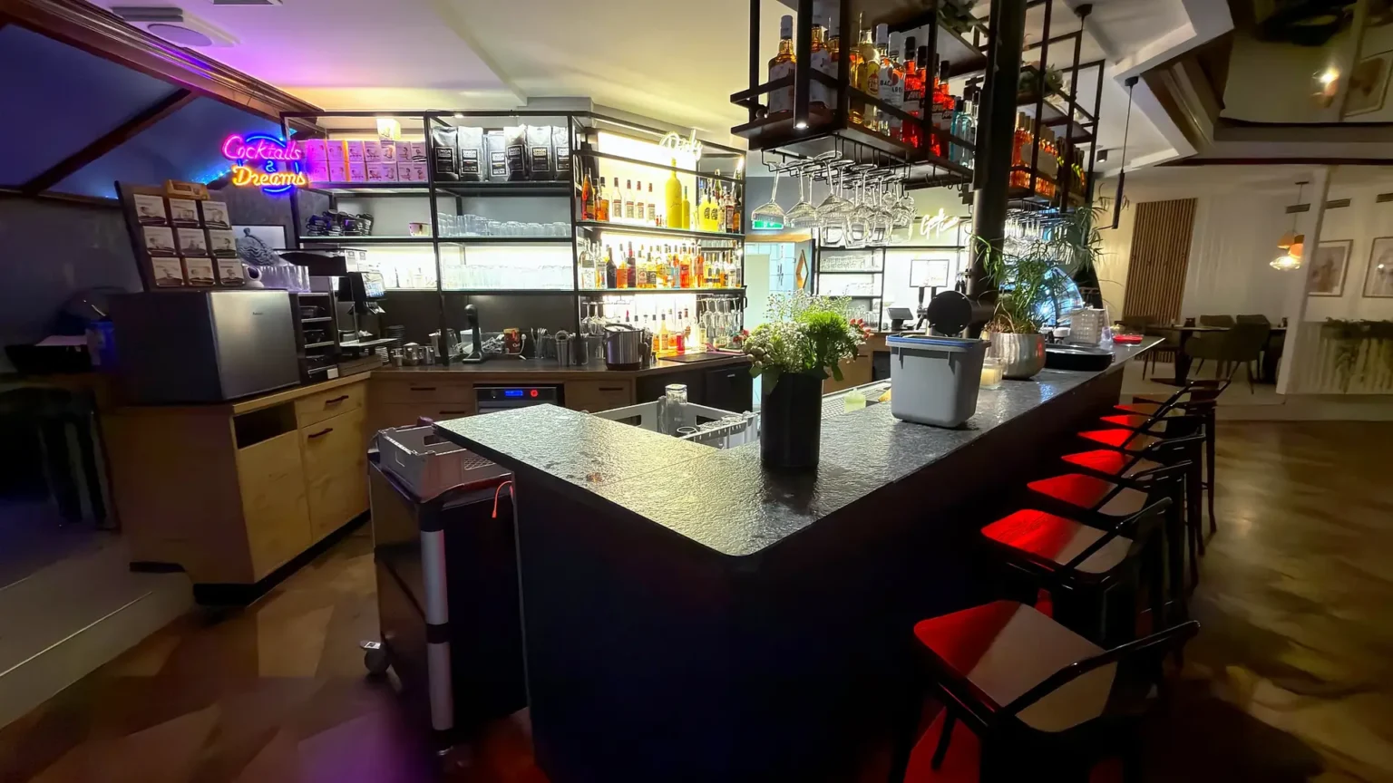 Bartheke des MIRA mit Cocktail-Neon und roten Barhockern